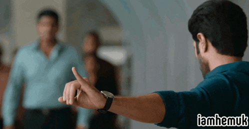 a man in a blue shirt is giving a thumbs up with a watch on his wrist