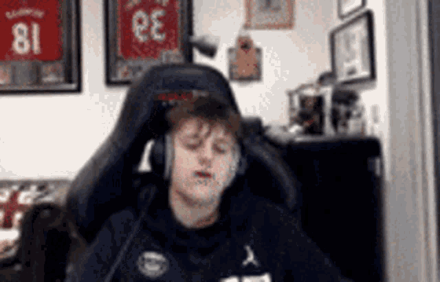 a man wearing headphones is sitting in a chair in front of a wall with jerseys on it .