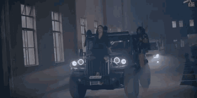 a woman is sitting on the hood of a jeep while a group of men are standing behind her .