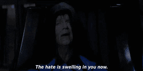 a man in a hooded jacket is sitting in a dark room and says `` the hate is swelling in you now '' .