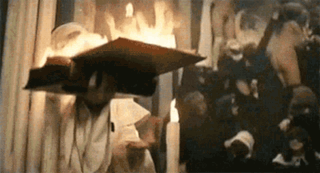 a man is holding a book that is on fire in front of a crowd of people .
