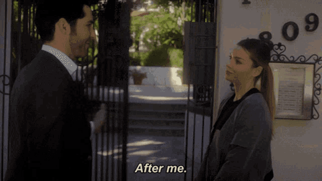 a man and a woman are standing in front of a gate and the woman says " after me "
