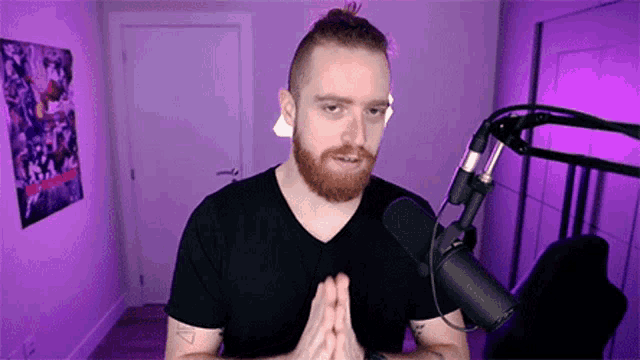 a bearded man is standing in front of a microphone in a purple room .