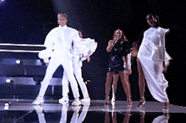 a group of people are dancing on a stage and one of them is wearing a white outfit