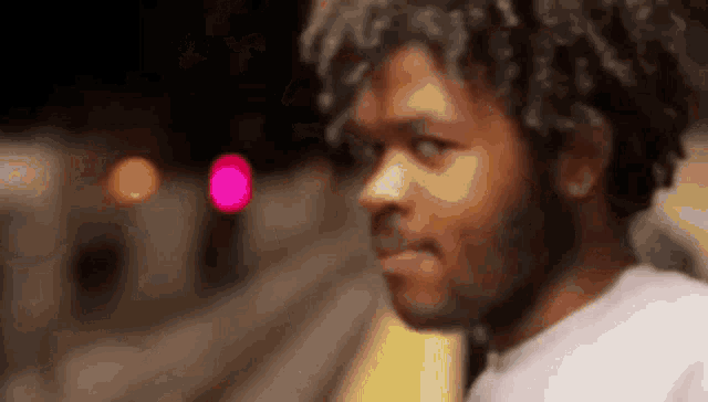 a man with curly hair and a beard is standing in front of a pink light .