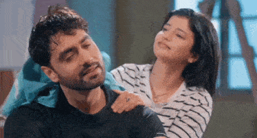 a man and a woman are sitting next to each other and the woman is putting her hand on the man 's neck .