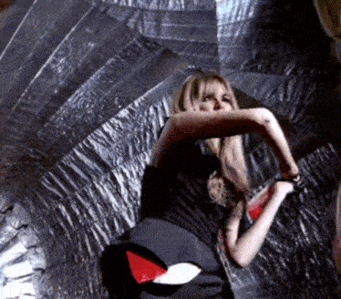 a woman in a black dress is dancing in front of a wall