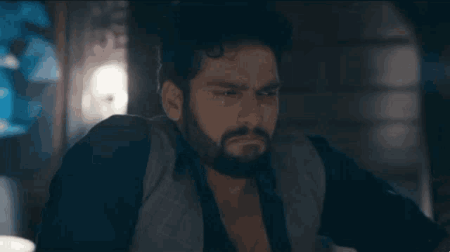 a man with a beard is sitting in a dark room looking at something .