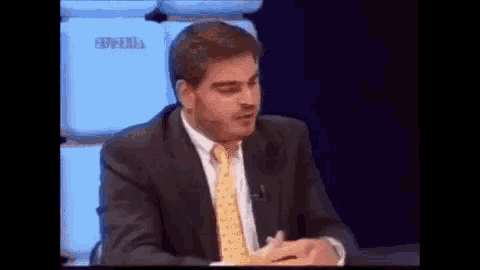 a man in a suit and tie is sitting at a table with a microphone on it