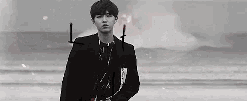 a black and white photo of a young man standing on the beach .