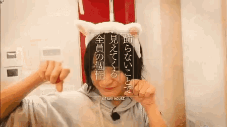 a woman is wearing a cat ear headband and holding a sign that says keyaki house