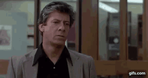a man in a suit and black shirt is standing in front of a window in a room .