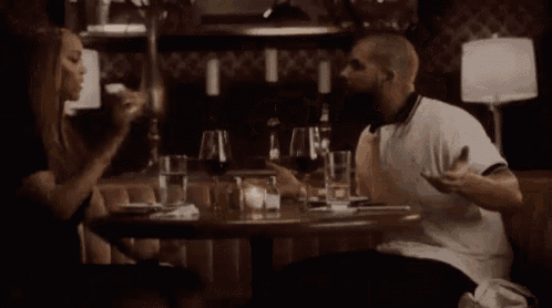 a man and a woman are sitting at a table in a restaurant having a drink .