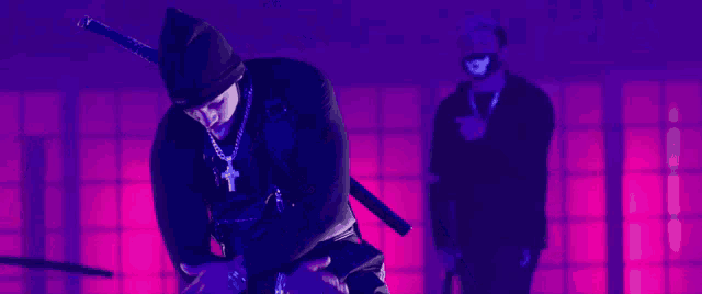 a man with a cross necklace is holding a sword in front of a purple background