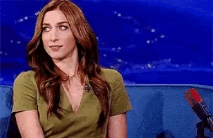 a woman in a green shirt is sitting in front of a microphone on a blue couch .