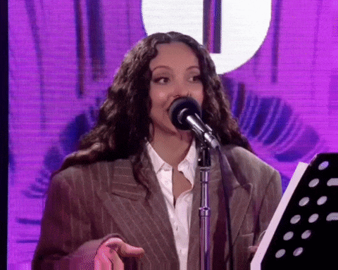 a woman in a suit is singing into a microphone while standing in front of a purple background .