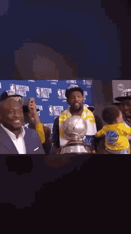 a baby in a golden state warriors shirt is being held by a man holding a trophy