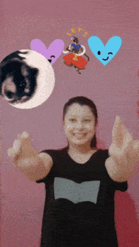 a woman in a black shirt stands in front of a pink wall with hearts and the word let 's