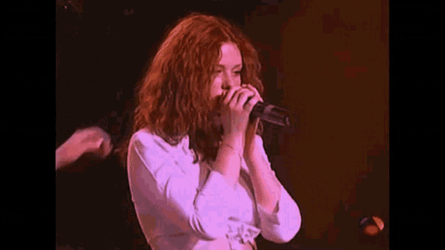a woman with red hair is singing into a microphone on a stage