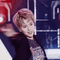 a young man with pink hair is standing on a stage with his arms outstretched .