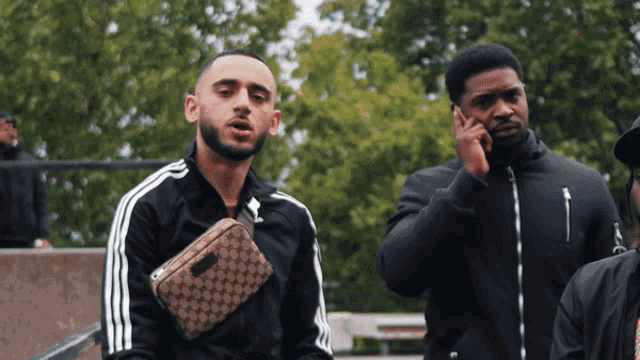a man talking on a cell phone next to another man with a gucci bag