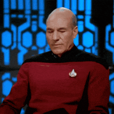 a bald man in a red and black uniform with a star trek badge on his chest