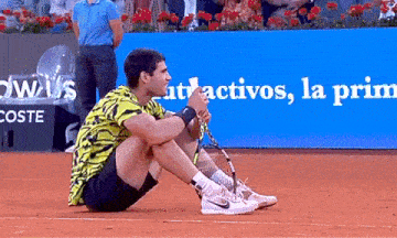 a man sits on the ground with a tennis racquet in front of a sign that says " activos "