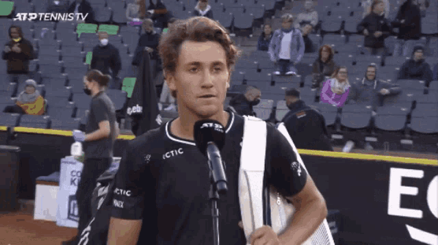 a man is talking into a microphone while wearing a black shirt that says ictic on it