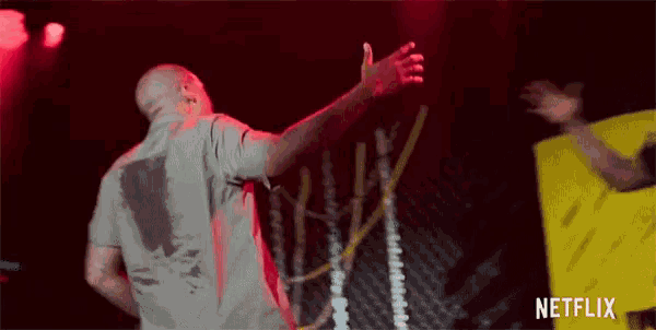 a man is standing on a stage with his arms outstretched in front of a yellow sign that says netflix .