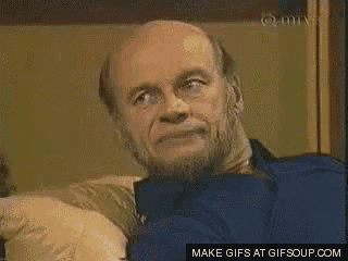 a bald man with a beard is sitting on a couch looking at the camera .