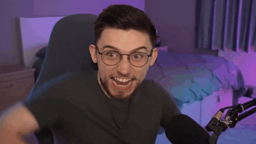 a man with glasses and a beard is smiling in front of a microphone