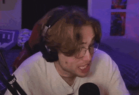 a young man wearing headphones and glasses is sitting in front of a microphone and making a funny face .
