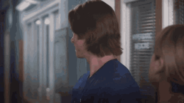 a man in a scrub top is standing next to a woman in a hallway .
