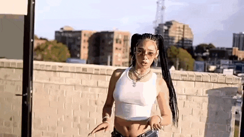 a woman in a white tank top and ponytail is standing on a rooftop .