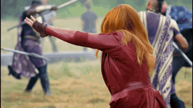 a woman in a red leather jacket is standing in a field holding a sword