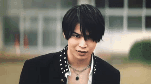 a young man wearing a black jacket and a necklace looks at the camera .