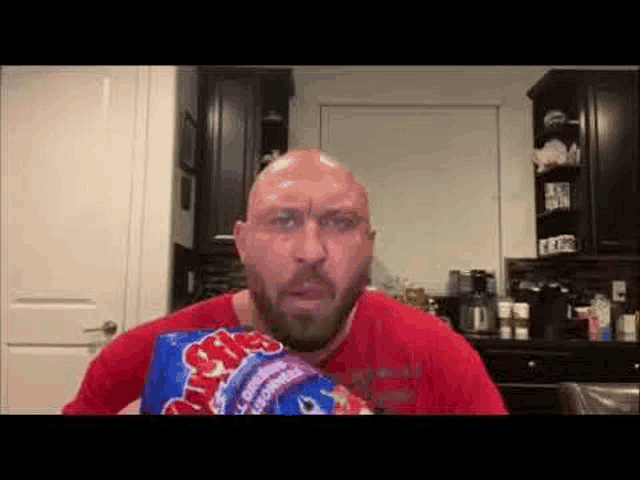 a bald man with a beard is holding a bag of m & ms .