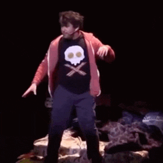 a man in a skull and crossbones shirt is standing on a stage with his hands in the air .