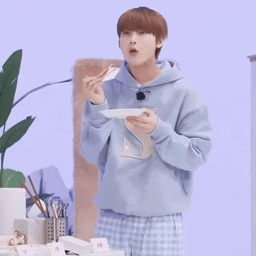 a young man in pajamas is standing in front of a table holding a plate .