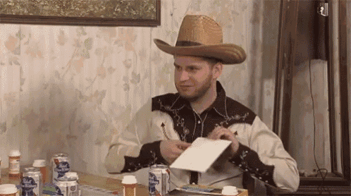 a man in a cowboy hat is sitting at a table with a notebook and a pen .