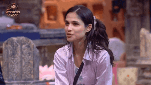 a woman is sitting in front of a sign that says weekend ka vaar
