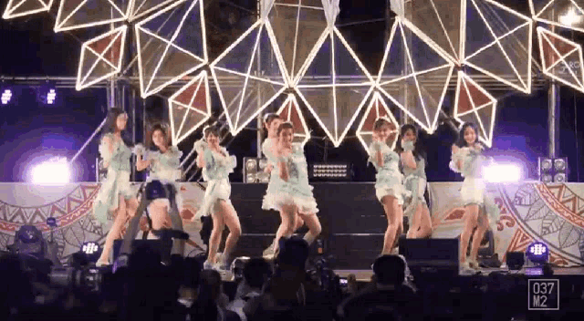 a group of women are dancing on a stage with a sign that says 037 m2