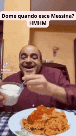 a man is sitting at a table with a plate of food and a spoon in his mouth ..
