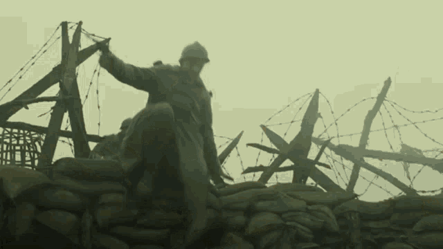 a soldier stands on top of a pile of sandbags surrounded by barbed wire