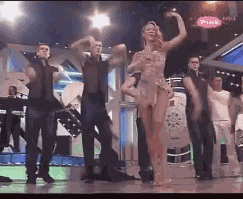 a group of people are dancing on a stage with a pink sign in the corner
