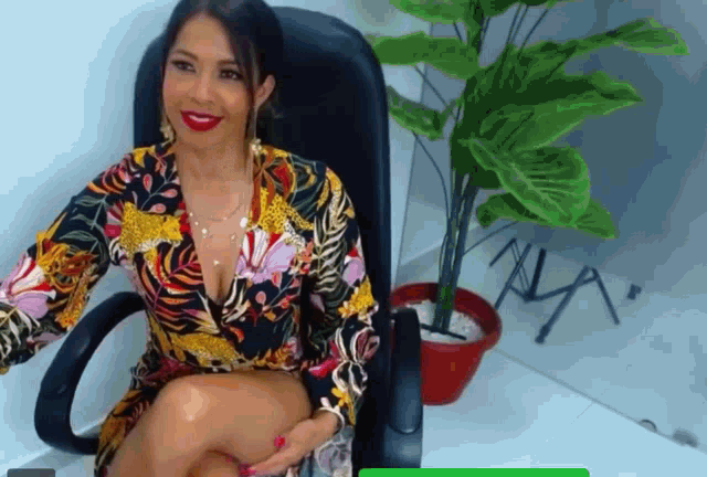 a woman in a colorful dress sits in an office chair next to a plant