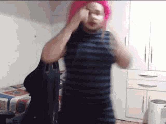 a woman with pink hair is dancing in a room while wearing a striped dress .