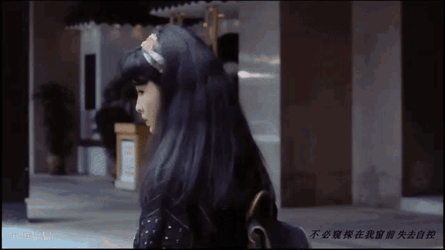 a woman with long black hair is walking down a street in front of a building