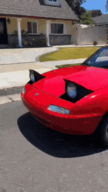 a red sports car is parked in front of a house with its headlights on .