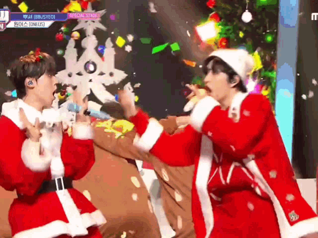 two men dressed as santa claus singing on a stage